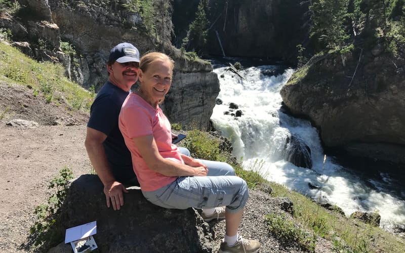 My mother and father sitting together on a rock above a waterfall, looking back at the camera.